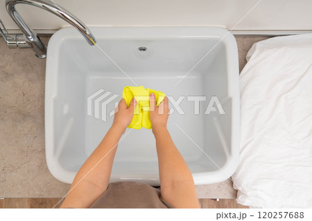 A person washing a bright yellow cloth in a utility sink with clean running water. A person washing a bright yellow cloth in a utility sink with clean running water. 120257688