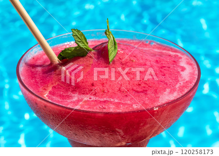 Chilled red drink with mint garnish by blue pool. Concept of summer refreshment and tropical relaxation Chilled red drink with mint garnish by blue pool. Concept of summer refreshment and tropical relaxation 120258173
