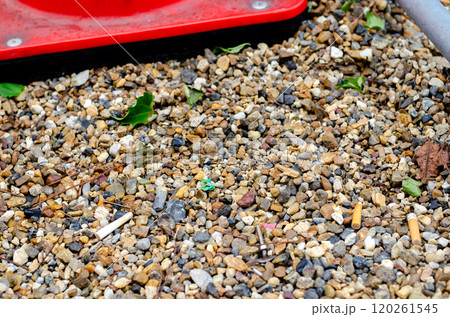 公園内の砂利に紛れるポイ捨てされたゴミたち 120261545