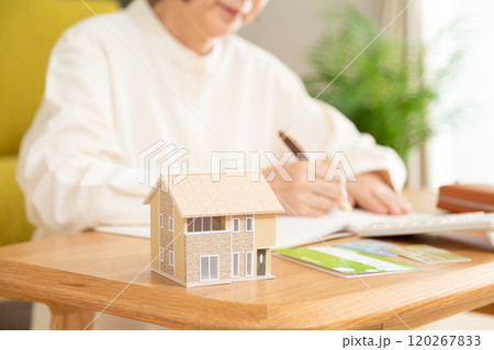 家計簿をつけるミドル〜シニア女性と家の模型 家計簿をつけるミドル〜シニア女性と家の模型 120267833