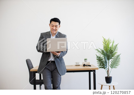 Smiling businessman working on laptop in modern office space 120270857