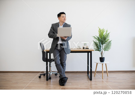 Confident businessman using laptop in modern office setting 120270858