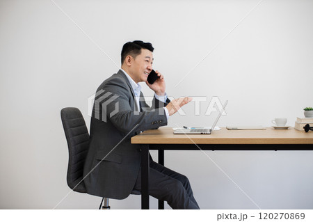Asian businessman multitasking with phone and laptop at modern office desk 120270869