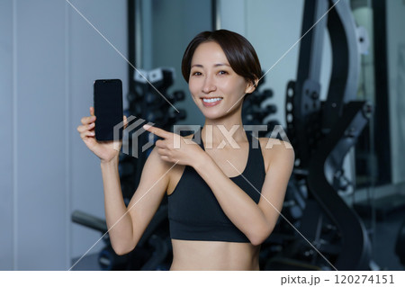 ジムでスマホを手にする笑顔の女性 ジムでスマホを手にする笑顔の女性 120274151