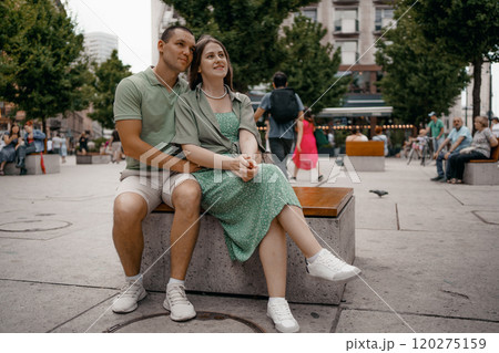 Couple enjoying a casual conversation on a bench outdoors in a city. A couple chats and smiles together while seated on a bench in city Warsaw. Poland. Couple in love visiting Warsaw. Couple enjoying a casual conversation on a bench outdoors in a city. A couple chats and smiles together while seated on a bench in city Warsaw. Poland. Couple in love visiting Warsaw. 120275159