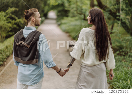 A beautiful couple's engagement portrait by the lovely trees. A stylish young couple, dressed in elegant attire, embraces each other in a lush green field, expressing love and connection. Warsaw. 120275192
