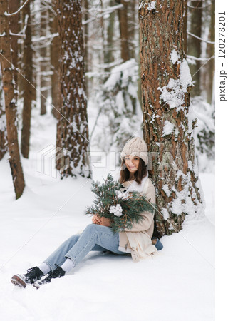 Woman is sitting in snow with bouquet of flowers in her lap. She is wearing hat and scarf 120278201