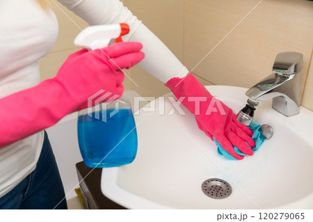 A woman is cleaning the bathroom sink with spray cleaner for hygiene and freshness 120279065