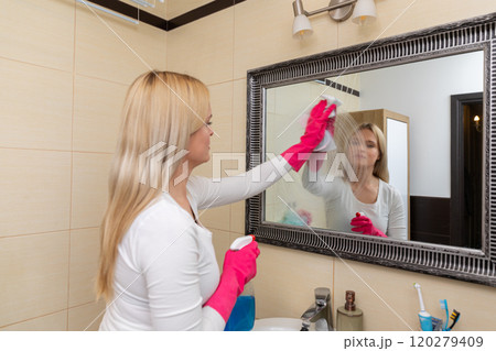 A woman diligently cleaning her bathroom mirror using a spray for a clear reflection 120279409