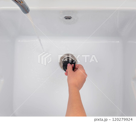 A person adjusting the drain plug in a utility sink with running water from a faucet for cleaning purposes. 120279924