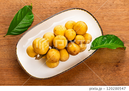 Top view of a bunch of ripe Long kong in brown ceramic tray with dark edge on wooden table. 120280547
