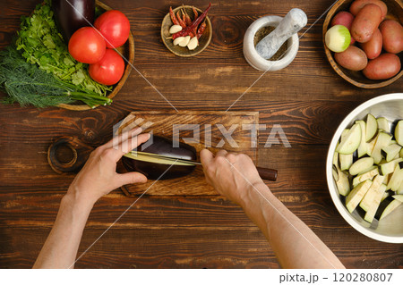 Unrecognizable person cuts an eggplant lengthwise on a chopping board Unrecognizable person cuts an eggplant lengthwise on a chopping board 120280807