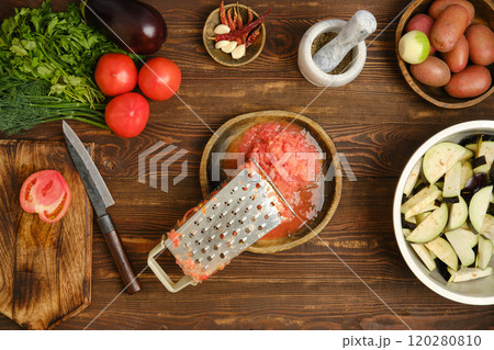 Grated fresh tomatoes and metal grater on a wooden bowl, top view 120280810