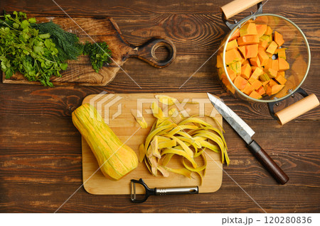 Preparing fresh butternut squash and herbs in a rustic kitchen setting during daylight 120280836