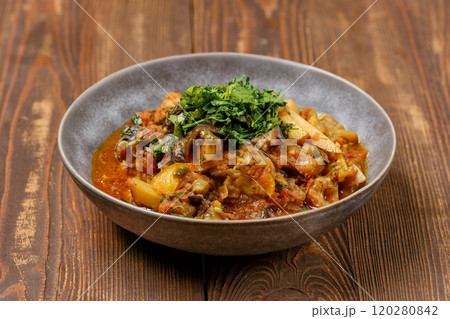 Hearty vegetable stew served in a rustic bowl garnished with fresh herbs on wooden table Hearty vegetable stew served in a rustic bowl garnished with fresh herbs on wooden table 120280842