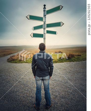 Rear view person stands at crossroad facing a signpost with multiple blank directional signs in a foggy open land. Different way choices, difficult decision, uncertainty concept 120282303