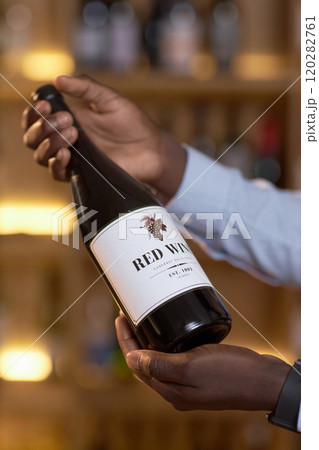 Vertical shot of bottle with white label full with red dry wine in male hands 120282761
