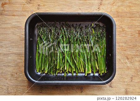 Roasted asparagus spears seasoned with salt and oil in baking tray placed on wooden surface 120282924