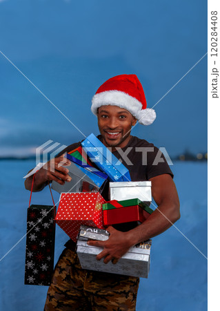 man holding gift boxes for christmas in the snow winter landscape and wearing red santa hat outside man holding gift boxes for christmas in the snow winter landscape and wearing red santa hat outside 120284408