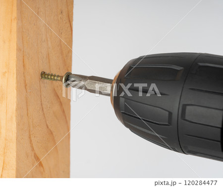 A screwdriver confidently screws a metal screw into a wooden board. A screwdriver confidently screws a metal screw into a wooden board. 120284477
