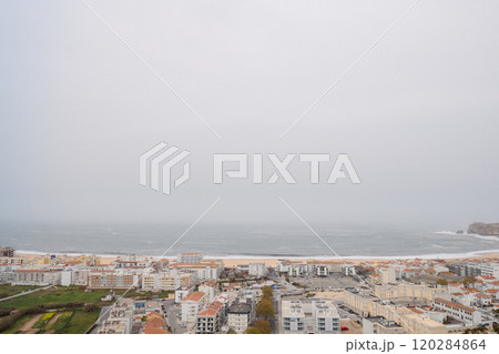 Panoramic view of a seaside town with red-tiled roofs, sandy beach, and ocean under a cloudy sky on a calm day 120284864