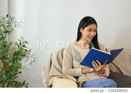Serene young woman reading a book, relaxing on a comfortable sofa Serene young woman reading a book, relaxing on a comfortable sofa 120288092