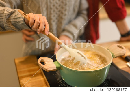 Close up of couple cooking pasta together in a warm kitchen during the festive season 120288177