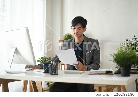 Adult businessman in suit analyzing reports in a modern office space Adult businessman in suit analyzing reports in a modern office space 120288186
