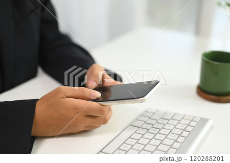 Close up of businesswoman using mobile phone next to computer keyboard at office desk 120288201