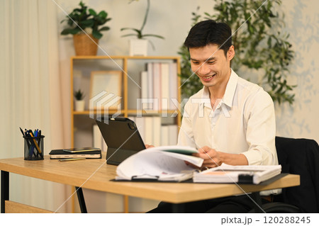 Smiling adult businessman analyzing financial reports and using digital tablet at desk 120288245