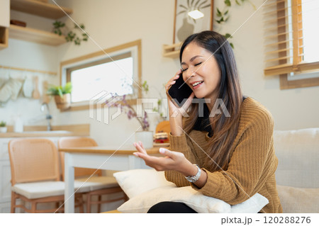 Smiling young adult woman enjoying a friendly phone chat in living room 120288276