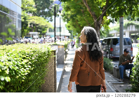 Back view of confident senior businesswoman strolling through urban greenery 120288279