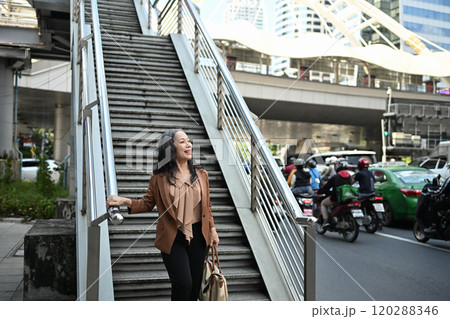 Confident senior woman walking down stairs exploring the city during daytime 120288346