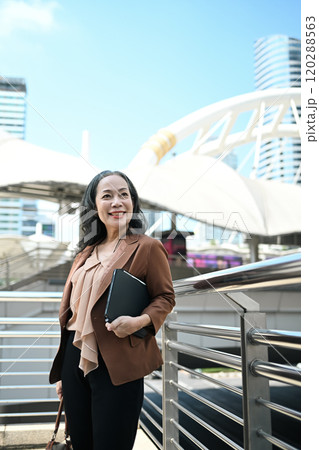 Portrait of elegant mature businesswoman standing in the city and looking upwards Portrait of elegant mature businesswoman standing in the city and looking upwards 120288563