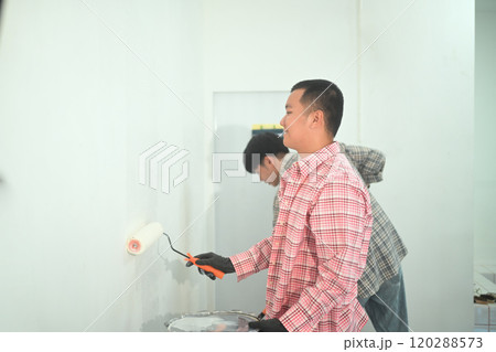 Young man painting a wall using a paint roller in newly renovated space. Home Improvement concept 120288573