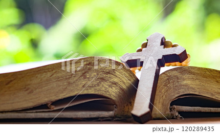 Brown wooden cross on an old open book symbolizing the spread of Jesus Christs love among Christians reflecting faith devotion and the importance of Christian teachings. 120289435