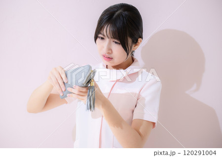 お金が金欠でなくて財布を見て困る看護師の女性 ピンクの背景 お金が金欠でなくて財布を見て困る看護師の女性 ピンクの背景 120291004