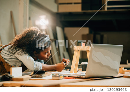 African American carpenter woman works on a wooden project using a laptop. utilize modern technology for designing new furniture, blending craftsmanship with digital tools, National Carpenters Day 120293468