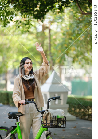 A woman is riding a bike and waving to someone A woman is riding a bike and waving to someone 120295343