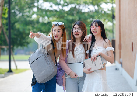 Three young women are walking down a sidewalk, each carrying a backpack 120295371