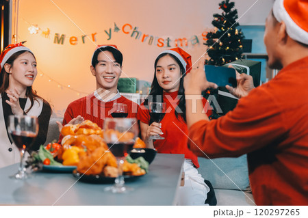 Group of young Asian man and women as friends having fun at a New Year's celebration, holding gift boxes standing by Christmas tree decoration, midnight countdown Party at home with holiday season. 120297265