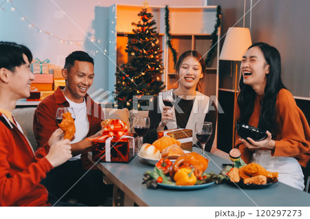 Group of young Asian man and women as friends having fun at a New Year's celebration, holding gift boxes standing by Christmas tree decoration, midnight countdown Party at home with holiday season. 120297273