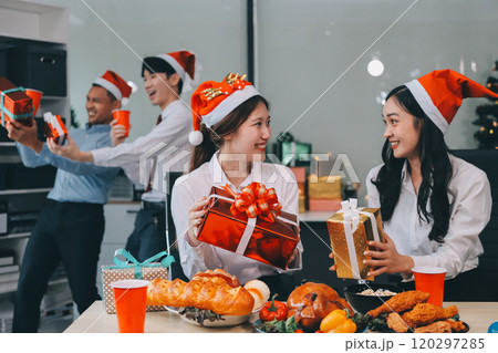 full length view of a group of business team wearing red Santa hat and exchange gift box together in the office for Christmas. 120297285