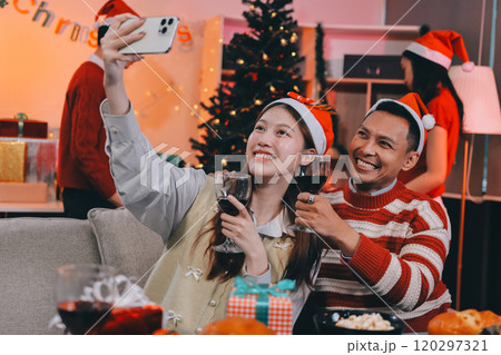 Group of happy Asian friends celebrating Christmas and decorate the Christmas tree indoors. Beauty woman with Christmas Gifts. New Year party. Woman hands decorate Christmas tree red ball, bauble. 120297321