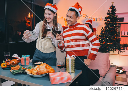 Group of happy Asian friends celebrating Christmas and decorate the Christmas tree indoors. Beauty woman with Christmas Gifts. New Year party. Woman hands decorate Christmas tree red ball, bauble. 120297324