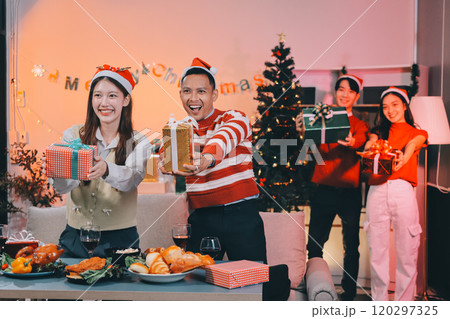 Group of happy Asian friends celebrating Christmas and decorate the Christmas tree indoors. Beauty woman with Christmas Gifts. New Year party. Woman hands decorate Christmas tree red ball, bauble. 120297325