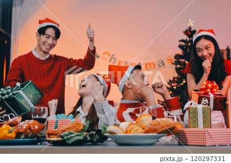 Group of happy Asian friends celebrating Christmas and decorate the Christmas tree indoors. Beauty woman with Christmas Gifts. New Year party. Woman hands decorate Christmas tree red ball, bauble. 120297331