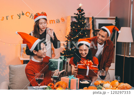 Group of young Asian man and women as friends having fun at a New Year's celebration, holding gift boxes standing by Christmas tree decoration, midnight countdown Party at home with holiday season. 120297333