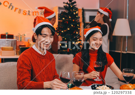 Group of young Asian man and women as friends having fun at a New Year's celebration, holding gift boxes standing by Christmas tree decoration, midnight countdown Party at home with holiday season. 120297338