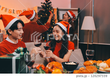 Group of young Asian man and women as friends having fun at a New Year's celebration, holding gift boxes standing by Christmas tree decoration, midnight countdown Party at home with holiday season. 120297339